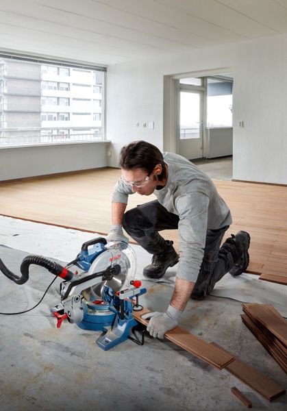GCM 254 Một người mặc đồ bảo hộ đang cắt sàn gỗ bằng cưa góc.