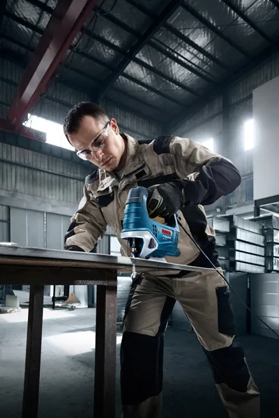 Một người mặc đồ bảo hộ đang sử dụng máy cưa lọng để cắt kim loại trong xưởng.