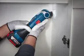 Một người mặc đồ bảo hộ đang sử dụng dụng cụ điện không dây để cắt tường tủ.