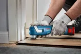 Một người mặc đồ bảo hộ sử dụng máy cắt đa năng không dây để cắt sàn gần cửa ra vào.