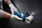 Một người mặc đồ bảo hộ đang cắt một ống nhựa màu trắng bằng máy cắt đa năng không dây.