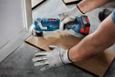 Người đeo thiết bị an toàn sử dụng máy cắt đa năng không dây để cắt sàn gần tường.