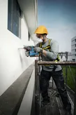 Một người mặc thiết bị an toàn đang khoan lỗ vào bên ngoài tòa nhà khi đang ở trên giàn giáo.