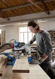 Một người mặc đồ bảo hộ đang cắt gỗ bằng máy cưa góc trong xưởng.