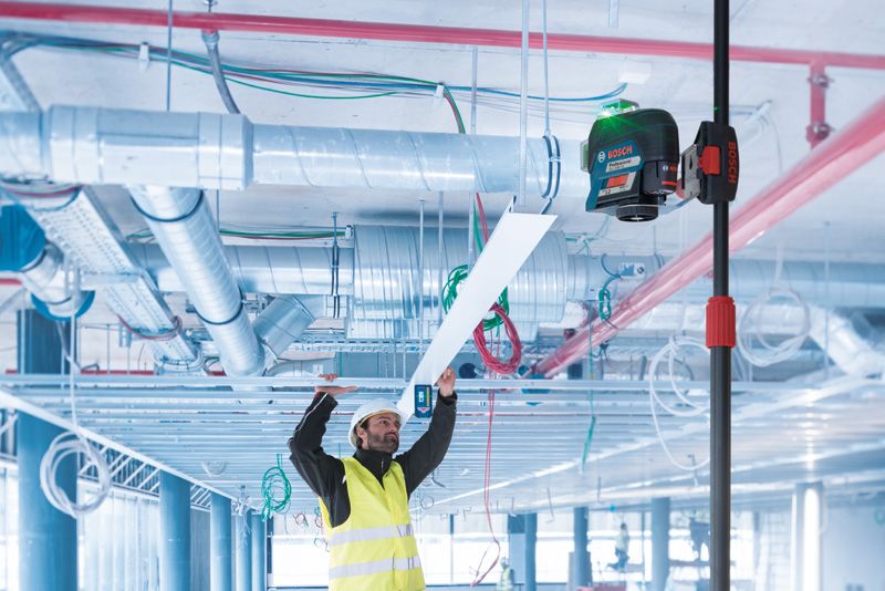 BT 350 Một người mặc thiết bị an toàn đang lắp đặt tấm trần bằng dụng cụ cân bằng laser trên một cột thu gọn.