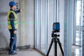 Một công nhân mặc đồ bảo hộ đang căn chỉnh khung tường bằng máy cân bằng laser.