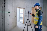 Một người mặc thiết bị an toàn đang vận hành máy cân bằng laser trên giá ba chân trong phòng bê tông.