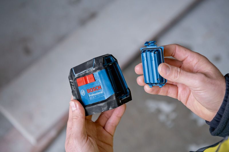 Người này cầm một dụng cụ cân bằng laser màu xanh và ngăn chứa pin của nó trong nhà.