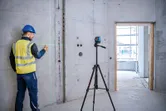 Một người mặc thiết bị an toàn đang đánh dấu bức tường bê tông bằng máy cân bằng laser trên chân máy.
