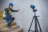 Một người mặc thiết bị an toàn đang đánh dấu bức tường bằng máy cân bằng laser trên chân máy.
