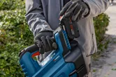 Một người đeo thiết bị an toàn đang lắp pin vào máy thổi lá không dây.