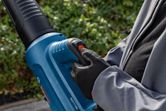 Một người mặc đồ bảo hộ đang vận hành máy thổi lá không dây ở ngoài trời.