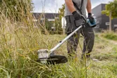 Một người mặc đồ bảo hộ đang cắt cỏ cao bằng máy cắt cỏ không dây.