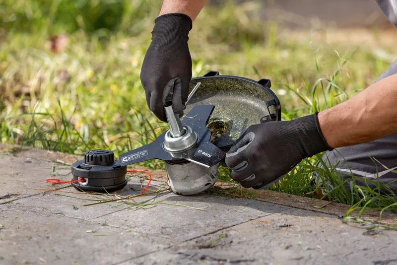 Một người đeo thiết bị an toàn đang điều chỉnh đầu máy cắt cỏ không dây trên bãi cỏ.