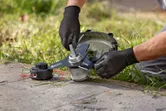 Một người đeo thiết bị an toàn đang điều chỉnh đầu máy cắt cỏ không dây trên bãi cỏ.