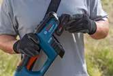 Một người đeo thiết bị an toàn đang lắp pin vào máy cắt cỏ không dây.
