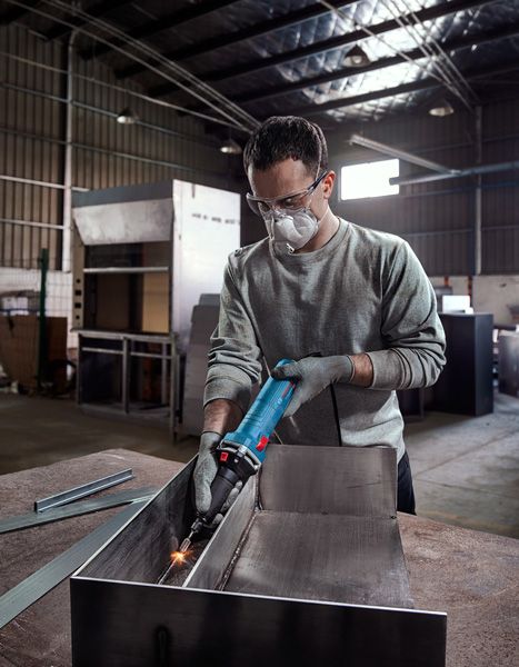 Một người mặc đồ bảo hộ đang mài kim loại bên trong một xưởng công nghiệp.