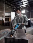 Một người mặc đồ bảo hộ đang mài kim loại bên trong một xưởng công nghiệp.