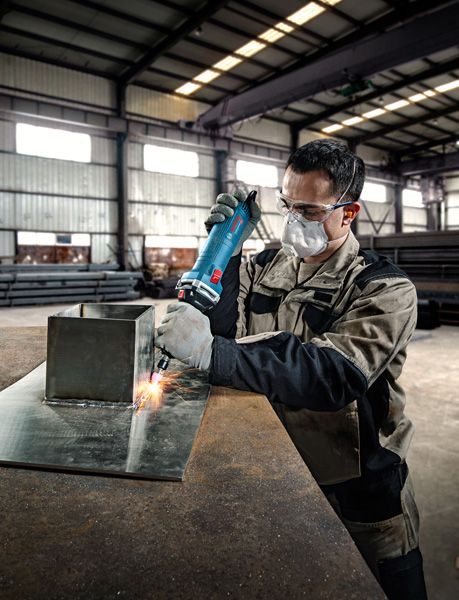 Một người mặc đồ bảo hộ đang sử dụng máy mài thẳng trên tấm kim loại.