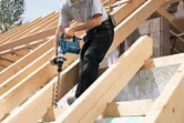 Một người đang khoan vào dầm gỗ trên mái nhà mà không đeo thiết bị an toàn.