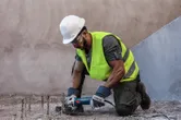 Một người mặc đồ bảo hộ đang cắt thanh thép lộ ra bằng máy mài góc.