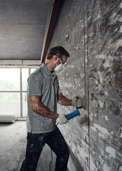 Một người mặc đồ bảo hộ đang sử dụng máy mài góc để cắt vào bức tường bê tông.