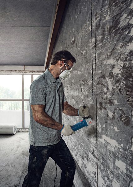 Một người mặc đồ bảo hộ đang sử dụng máy mài góc để cắt vào bức tường bê tông.