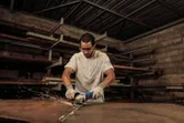 Một người mặc đồ bảo hộ đang mài một tấm kim loại bằng máy mài góc.