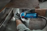 Một người mặc đồ bảo hộ đang mài mối hàn kim loại bằng máy mài thẳng.