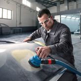 Một người mặc thiết bị an toàn đang sử dụng máy chà nhám quỹ đạo ngẫu nhiên trên mui xe ô tô.