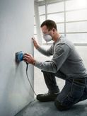 Một người mặc đồ bảo hộ đang chà nhám tường bằng máy chà nhám quỹ đạo.