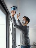 Một người mặc đồ bảo hộ đang chà nhám mép trần nhà bằng máy chà nhám quỹ đạo.