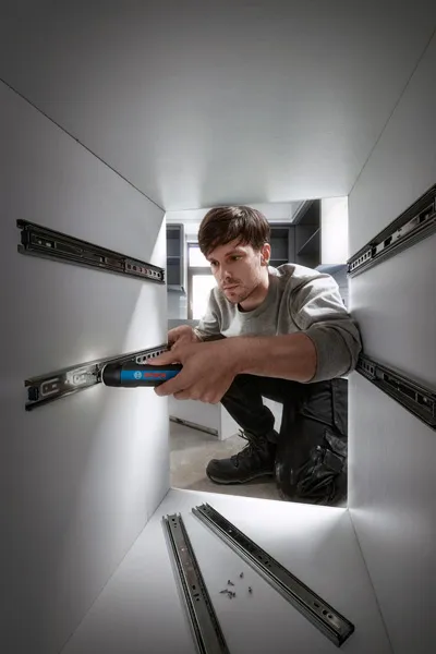 Một người sử dụng tua vít không dây để lắp thanh trượt ngăn kéo bên trong tủ.