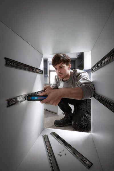 Một người sử dụng tua vít không dây để lắp thanh trượt ngăn kéo bên trong tủ.