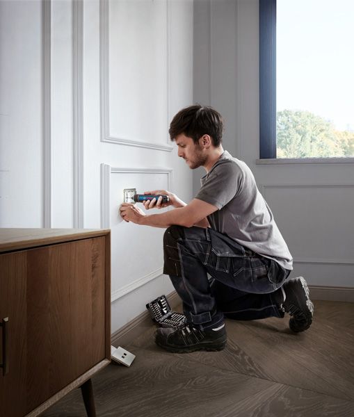 Một người đang lắp nắp ổ cắm điện bằng tua vít không dây.