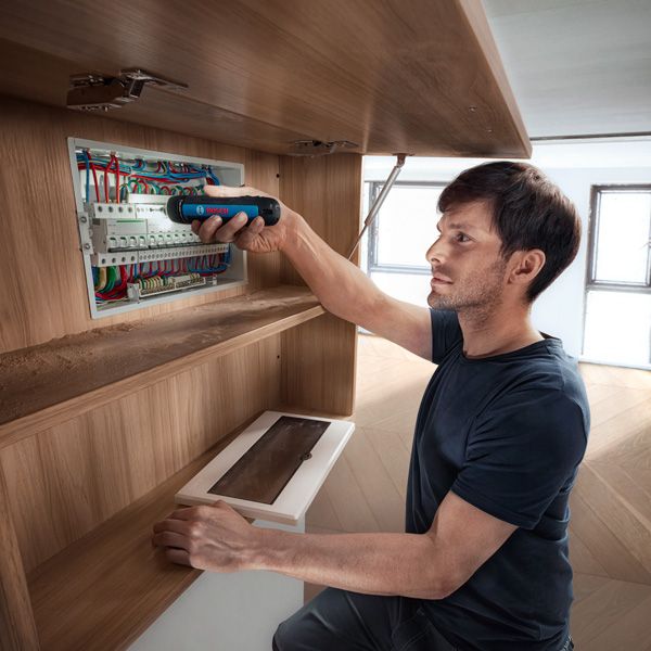 Một người đang cố định dây điện trong bảng điện bằng tua vít không dây.