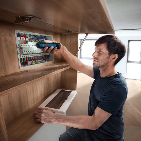 Một người đang cố định dây điện trong bảng điện bằng tua vít không dây.