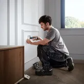 Một người sử dụng tua vít không dây để lắp nắp ổ cắm điện.
