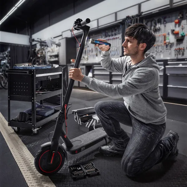 Một người đang quỳ xuống và sử dụng tua vít không dây để sửa chữa một chiếc xe tay ga điện.