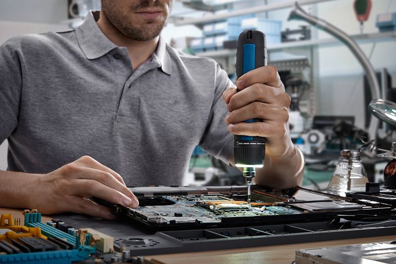 Người sử dụng tua vít không dây để lắp ráp các linh kiện điện tử trên bảng mạch.