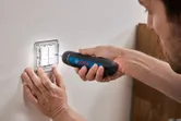 Một người sử dụng tua vít không dây để vặn chặt ốc vít trên bảng công tắc đèn.