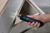 Một người sử dụng tua vít không dây để lắp ngăn kéo tủ bằng kim loại.