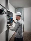 Người đeo thiết bị an toàn sử dụng máy khoan không dây trên bảng điện.