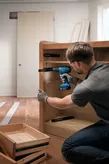Người đeo thiết bị an toàn đang lắp thanh trượt ngăn kéo tủ bằng máy khoan không dây.