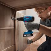 Một người mặc đồ bảo hộ sử dụng máy khoan không dây để lắp bản lề tủ.