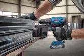 Một người mặc đồ bảo hộ sử dụng máy khoan không dây để siết chặt các thanh kim loại.
