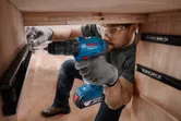 Một người mặc đồ bảo hộ đang lắp thanh trượt ngăn kéo bằng máy khoan không dây.