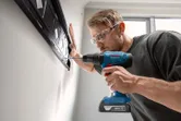 Một người mặc thiết bị an toàn khoan vào tường để lắp giá đỡ.