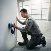 Một người mặc đồ bảo hộ đang chà nhám tường bằng máy chà nhám điện.