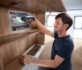 Một người sử dụng tua vít không dây để vặn chặt các thành phần trong bảng điện.